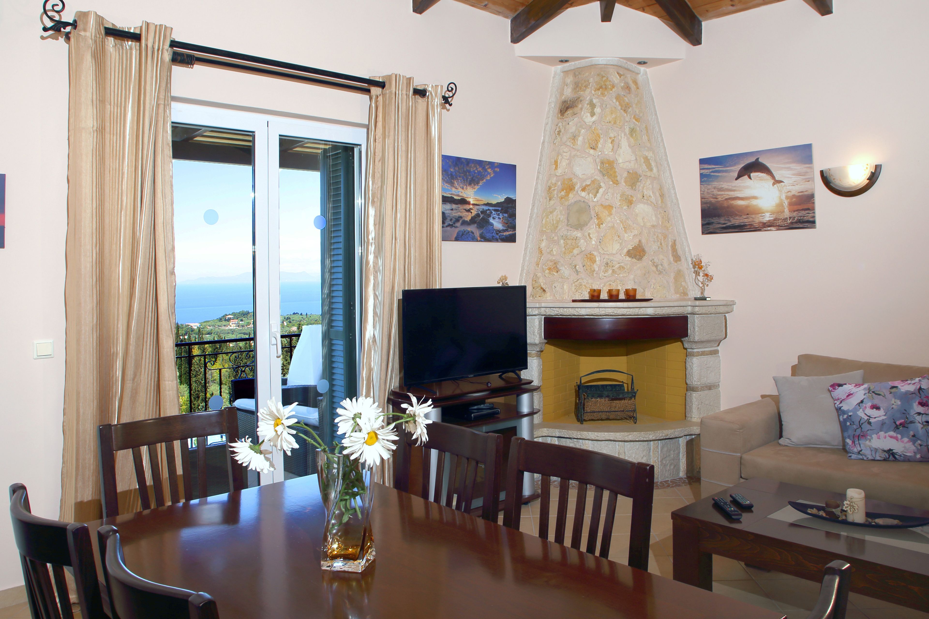 A dining area with a table, chairs, a vase with flowers, a television, and a fireplace.