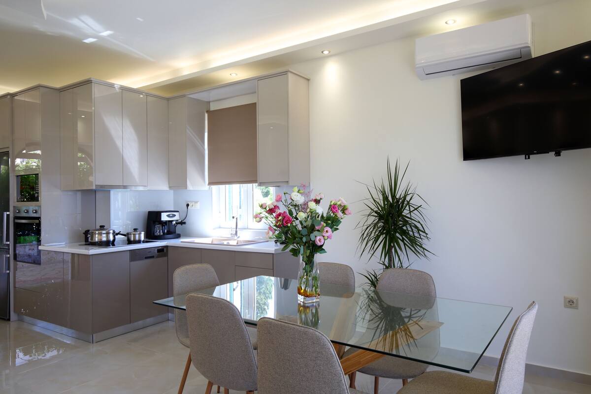 Una cocina moderna con comedor, que incluye una mesa de vidrio, sillas y un florero con flores.