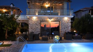 Un bâtiment en pierre de deux étages, doté d’une piscine, d’un espace extérieur aménagé et d’un balcon avec des garde-corps en verre.
