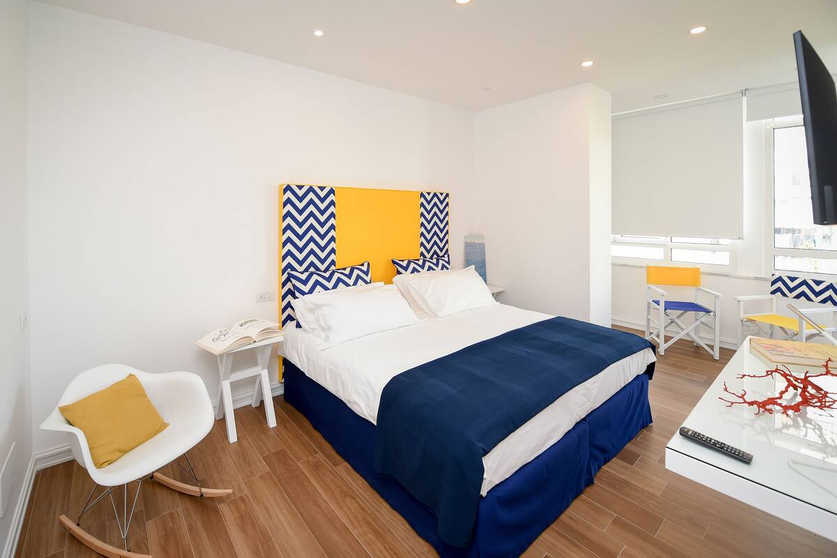 A modern hotel room with a bed, a desk, a chair, and a TV.