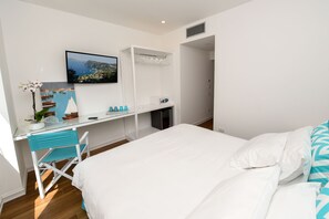 Un dormitorio con una cama, un escritorio con computadora, una silla y un televisor en la pared.