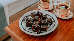 Una taula de fusta amb un plat de brownies i dues tasses de cafè.