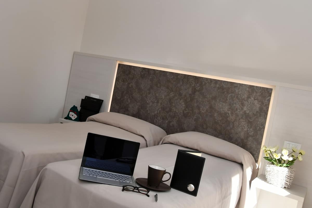 A hotel room with two beds, a laptop, a mug, glasses, and a small plant.
