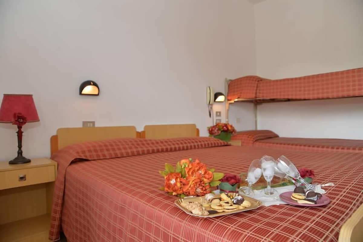 A hotel room with a bed, a nightstand, a lamp, a wall-mounted light, and a bedside table with a floral arrangement.