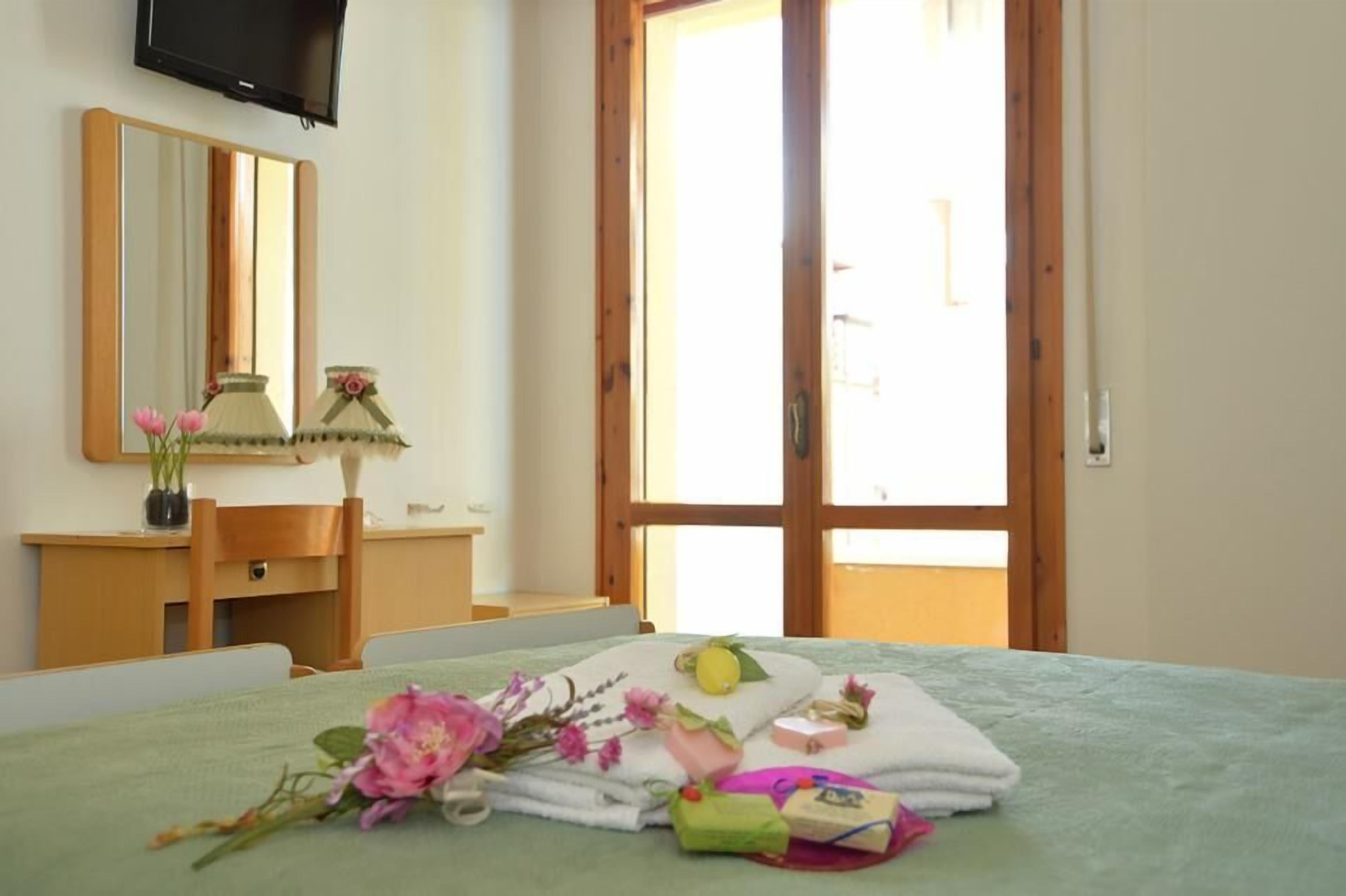 A bedroom with a bed, a bedside table, a mirror, and a window.