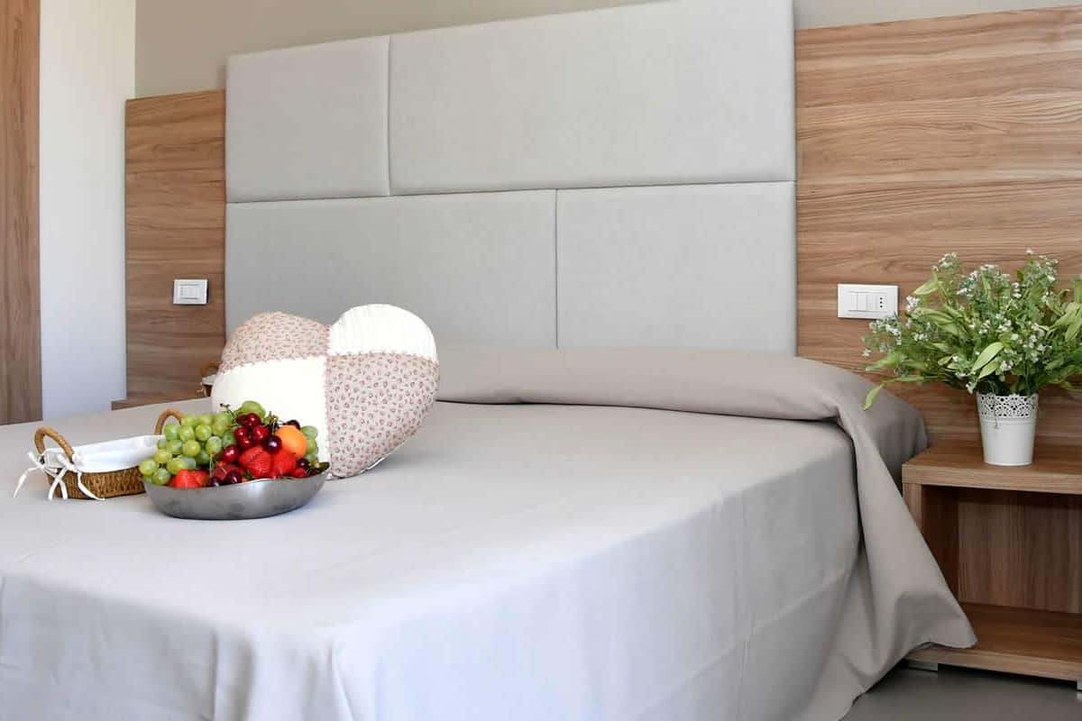 A modern bedroom with a bed, bedside table, chair, and a fruit bowl.