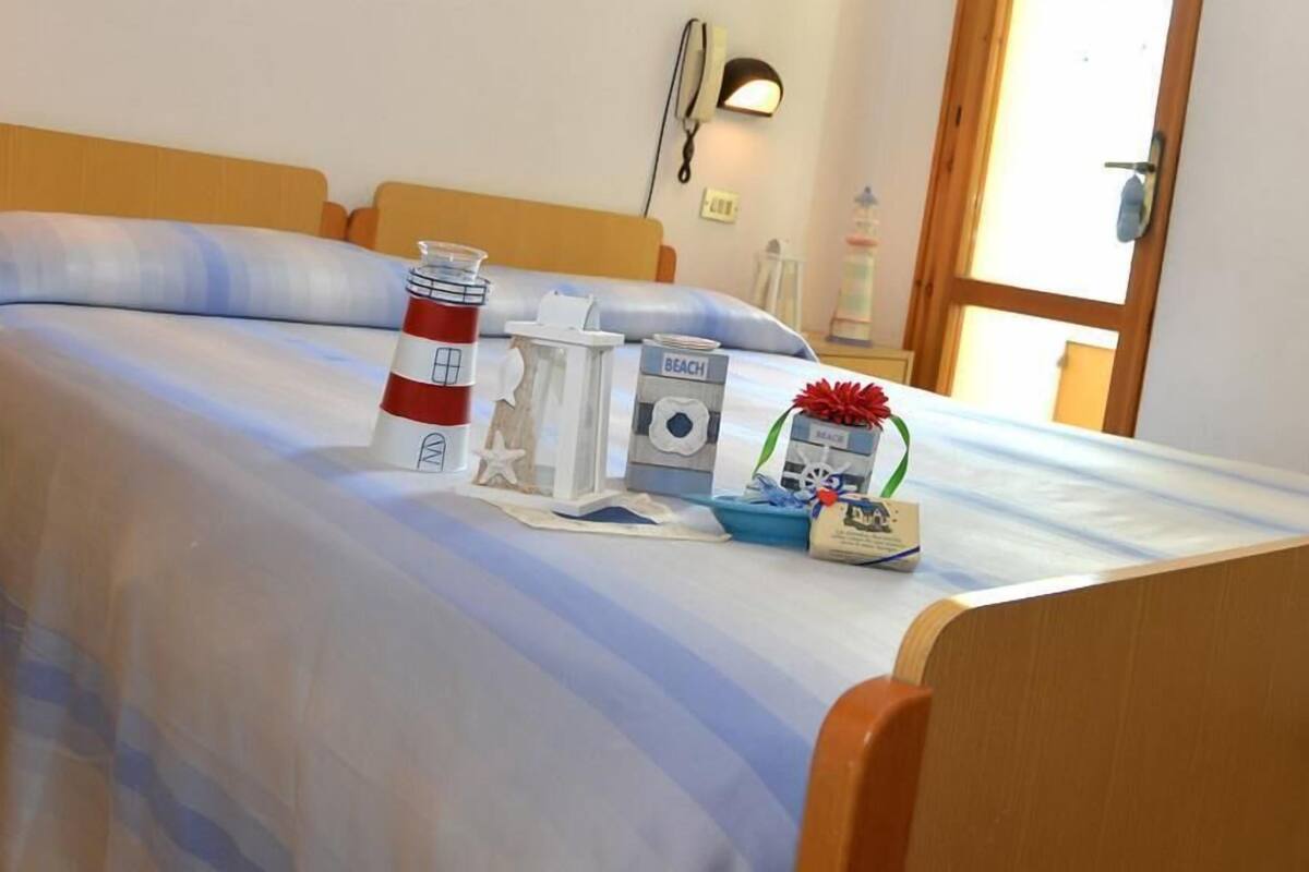 A bed with a striped blue and white bedspread, a small table with a lighthouse model, a beach-themed box, and a small decorative item.