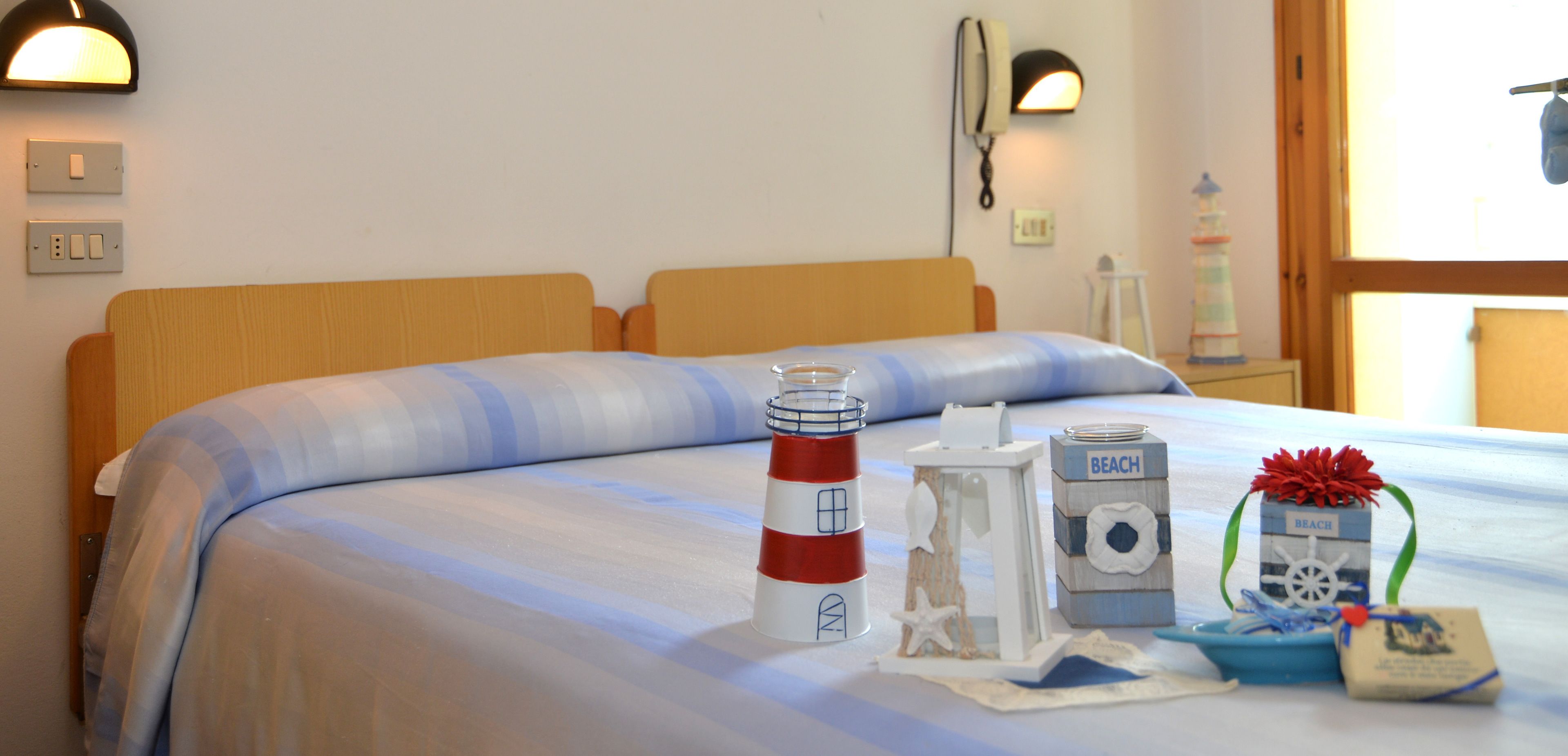 A bed with a striped blue and white bedspread, a red and white lighthouse decoration, a small lighthouse model, and a 'BEACH' themed box.