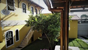 A yellow building with a staircase leading to a door, a tree in the yard, and a white wall with a window. - Vila do Sossego (Cabo Frio)