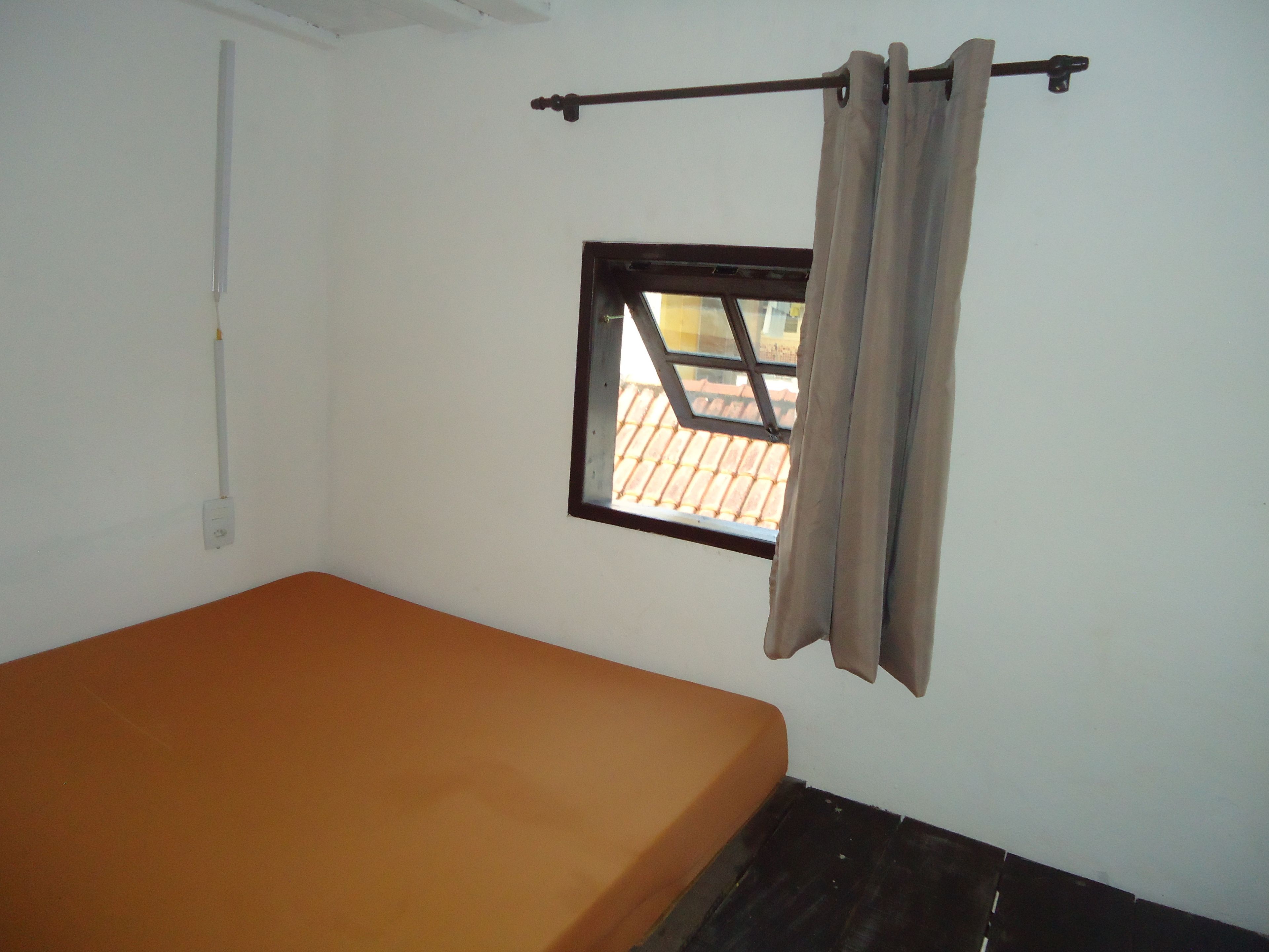 A small, single-bed room with a window and a curtain rod.