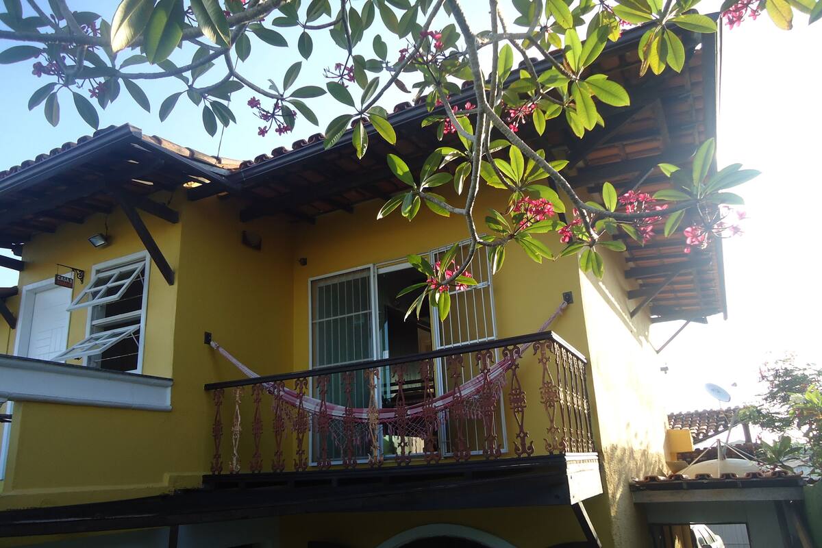 A yellow building with a balcony, a hammock, and a car parked in front.