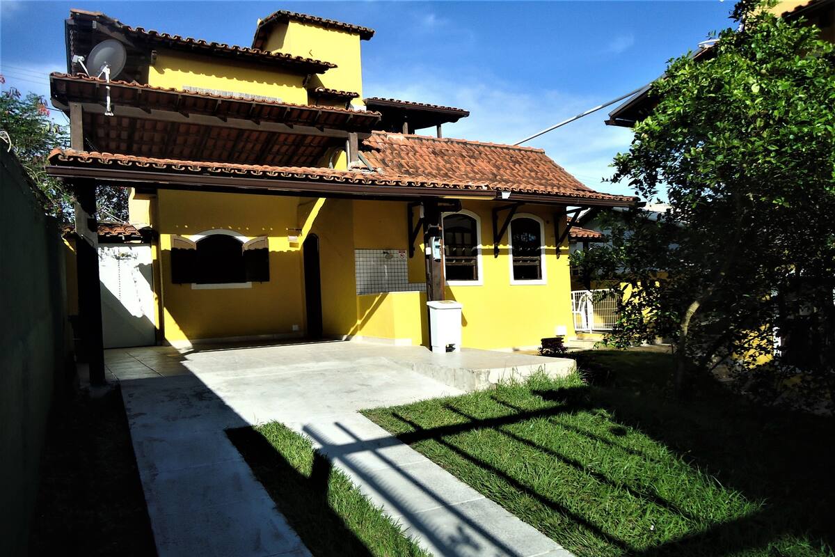 A yellow house with a tiled roof, a concrete driveway, and a well-maintained lawn.