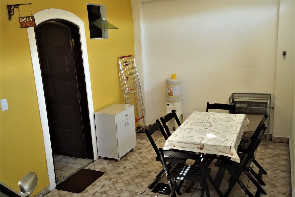A dining area with a table covered in a tablecloth, surrounded by chairs. There is a water dispenser and a small refrigerator in the room.