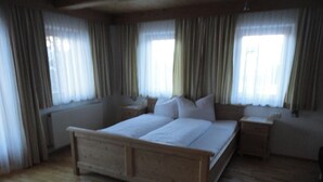 A bedroom with a wooden bed, two bedside tables, a radiator, and curtains. - Apartments Klammerhof (Hainzenberg)