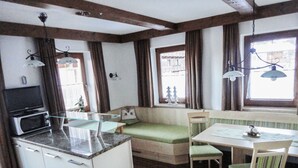 A compact kitchen with a microwave, a glass-top table, a bench, and a dining table with chairs. - Apartments Klammerhof (Hainzenberg)