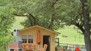 A wooden cabin with a patio area, a swing set, and a cow in the background. - Apartments Klammerhof (Hainzenberg)