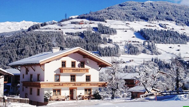A two-story chalet with a balcony, surrounded by snow-covered trees and mountains. - Apartments Klammerhof (Hainzenberg)