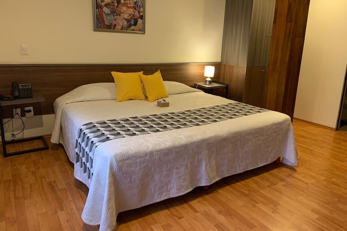 A hotel room with a large bed, two yellow pillows, a bedside table with a lamp, and a wall-mounted painting.