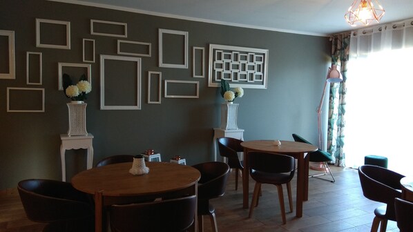 A dining area with a wooden table and chairs, a decorative wall with framed patterns, and a vase with flowers. - ALLuar Lodge (Angra do Heroismo)