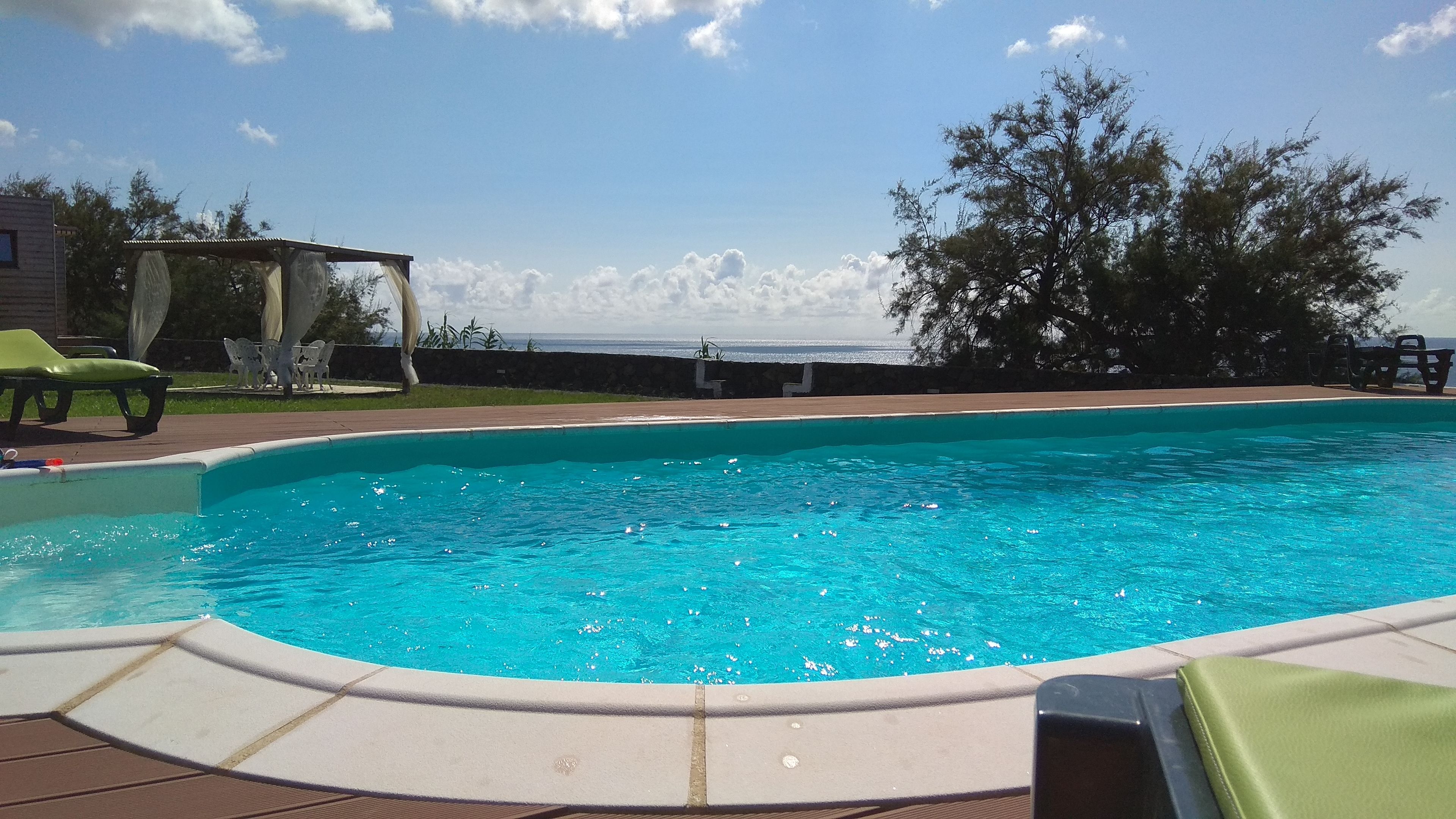 Piscina com água azul cristalina, rodeada por um deck com espreguiçadeiras e uma pérgola.