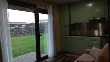 Een keuken met groene kastjes, een roestvrijstalen afzuigkap en een schuifdeur naar een grasveld buiten.