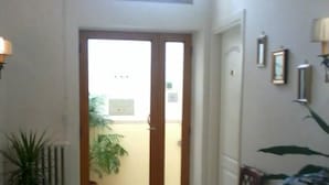 A living room with a sofa, a coffee table, a rug, and a dining table with chairs. There is a large window and a door leading to an outdoor area with a plant. - B&B Michael (Monte Sant'Angelo)