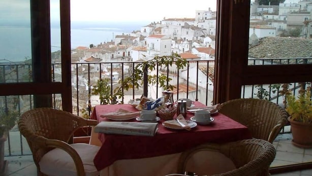 A balcony with wicker chairs, a table set for two, and a view of a coastal town. - B&B Michael (Monte Sant'Angelo)