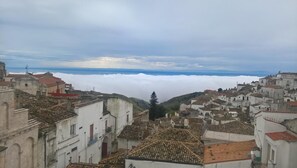 A town with historic buildings, a church, and a view of the sea through clouds. - B&B Michael (Monte Sant'Angelo)