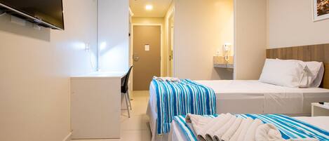 A hotel room with a desk, two beds, a TV, an air conditioner, and a bathroom visible through an open door.