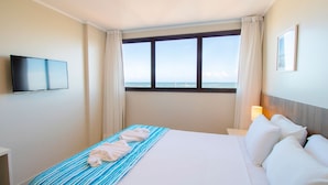 A hotel room with a bed, a TV mounted on the wall, a window with curtains, and a bedside lamp. - Acqua Inn (Maceió)