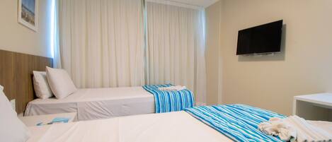 A hotel room with two beds, a flat-screen TV, and a window with sheer curtains.