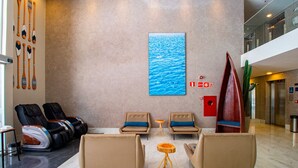A lobby with massage chairs, a wooden table, and a large painting of water. - Acqua Inn (Maceió)