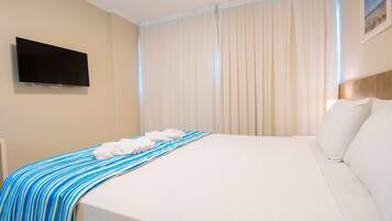 Habitación de hotel con cama, televisor de pantalla plana en la pared y ventana con cortinas de gasa.