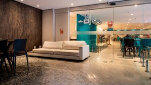 A modern hotel lobby with a sofa, chairs, and a glass partition leading to a dining area. - Acqua Inn (Maceió)