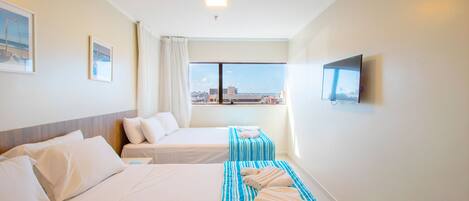 A hotel room with two beds, a TV, and a window with a city view.