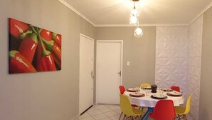 Zona pranzo con tavolo rotondo, sedie colorate, un quadro e una lampada a sospensione.