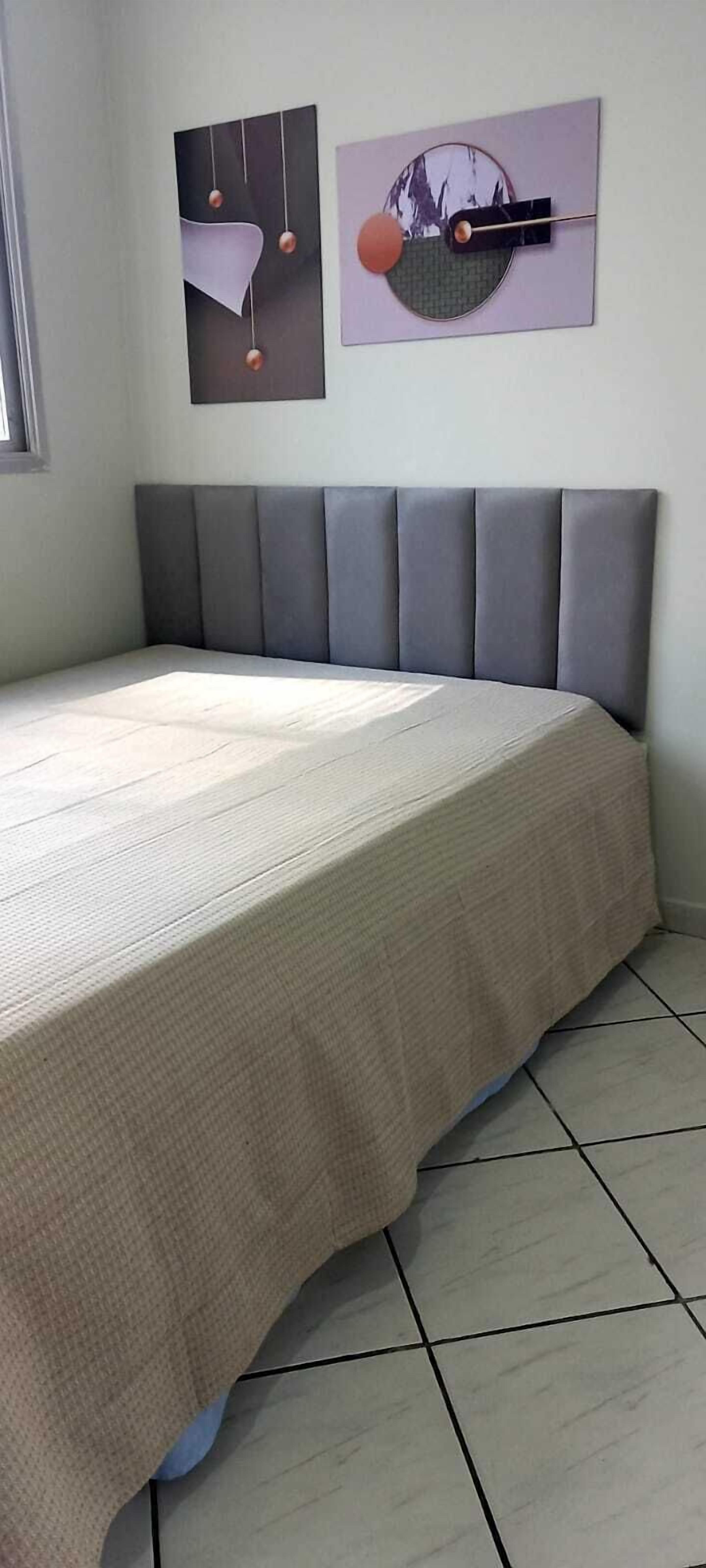 A bedroom with a bed, grey padded headboard, and two wall-mounted artworks.