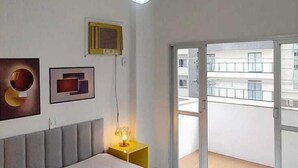 Una camera da letto con un letto grande, una ventola a soffitto, un comodino con una lampada e vista sul balcone esterno.