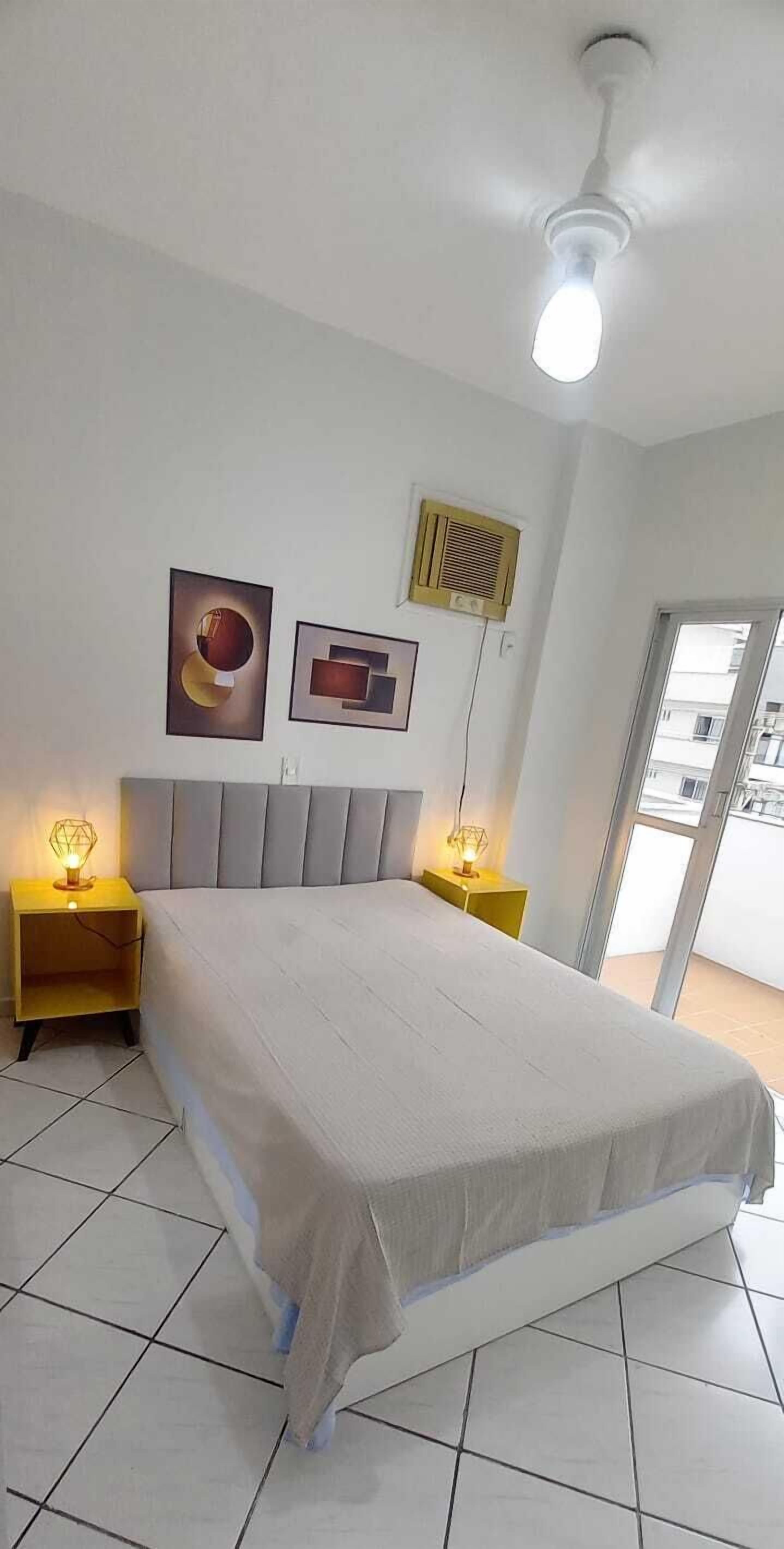A bedroom with a bed, two bedside tables with lamps, a ceiling fan, and two wall-mounted air vents.