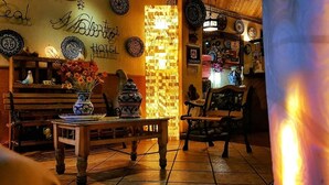 Um lobby de hotel acolhedor com um banco de madeira, uma mesa com um vaso de flores e uma parede decorada com pratos e uma placa que diz "Hotel".