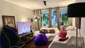 Una sala de estar con televisor, sofá, sillón y un asiento informal tipo puff.