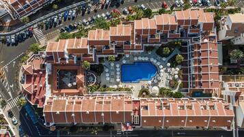 Vista aérea de un hotel con piscina, rodeado de zonas de estar al aire libre y varias plantas de habitaciones con techos de tejas rojas.