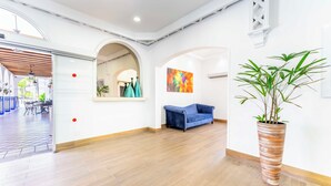 Una habitación amplia con suelo de madera, un sofá azul, una planta grande en maceta y un cuadro abstracto colorido en la pared.