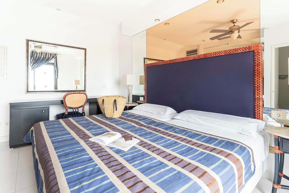 A hotel room with a bed, a desk, a chair, a mirror, and a ceiling fan.