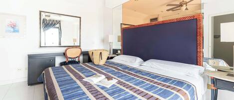 A hotel room with a bed, a desk, a chair, a mirror, and a ceiling fan.