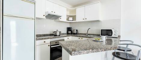A modern kitchen with white cabinets, a granite countertop, a microwave, a coffee maker, and a sink.