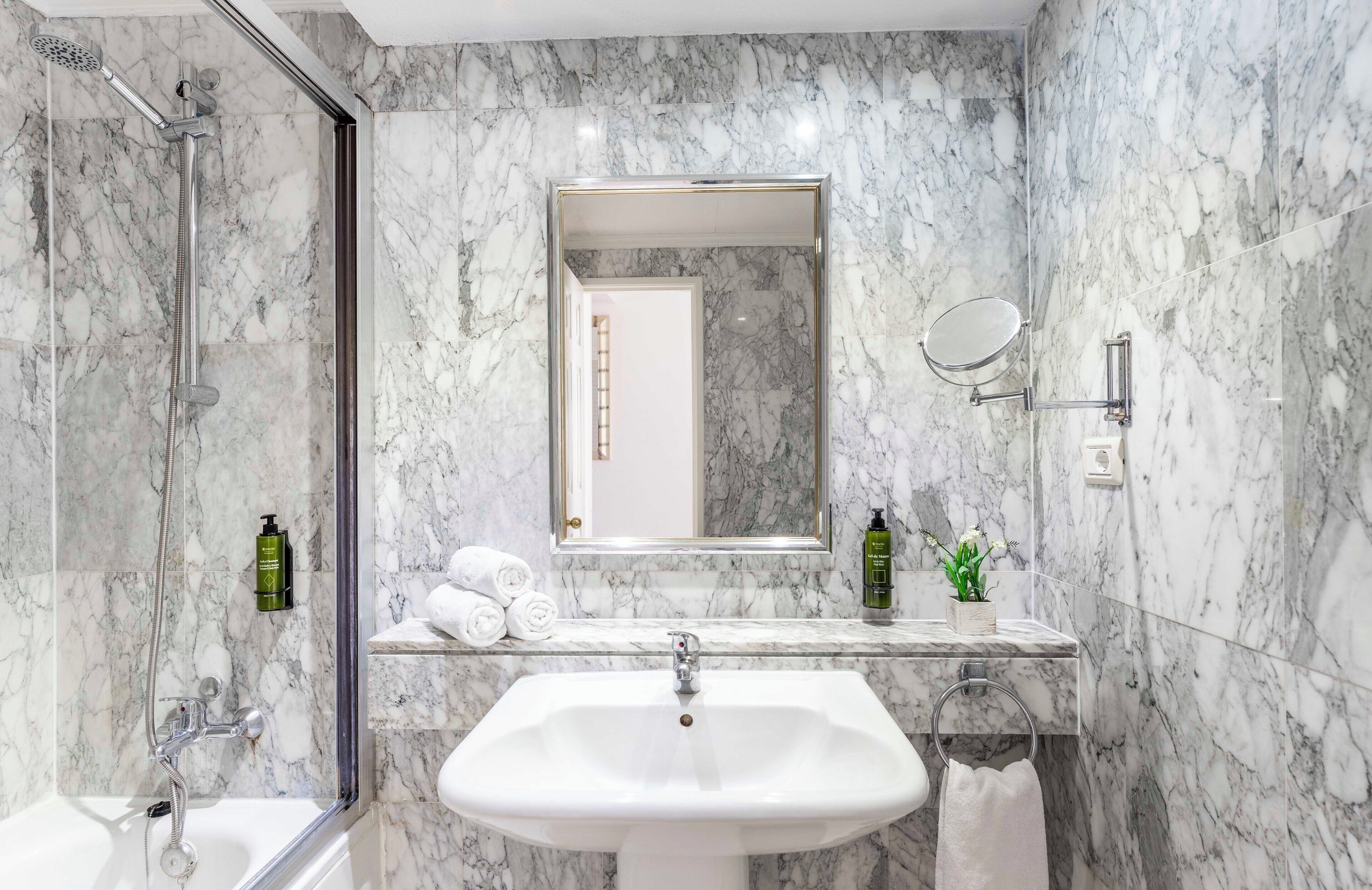 Une salle de bain moderne avec un mur en marbre, un grand miroir, un lavabo et une douche.