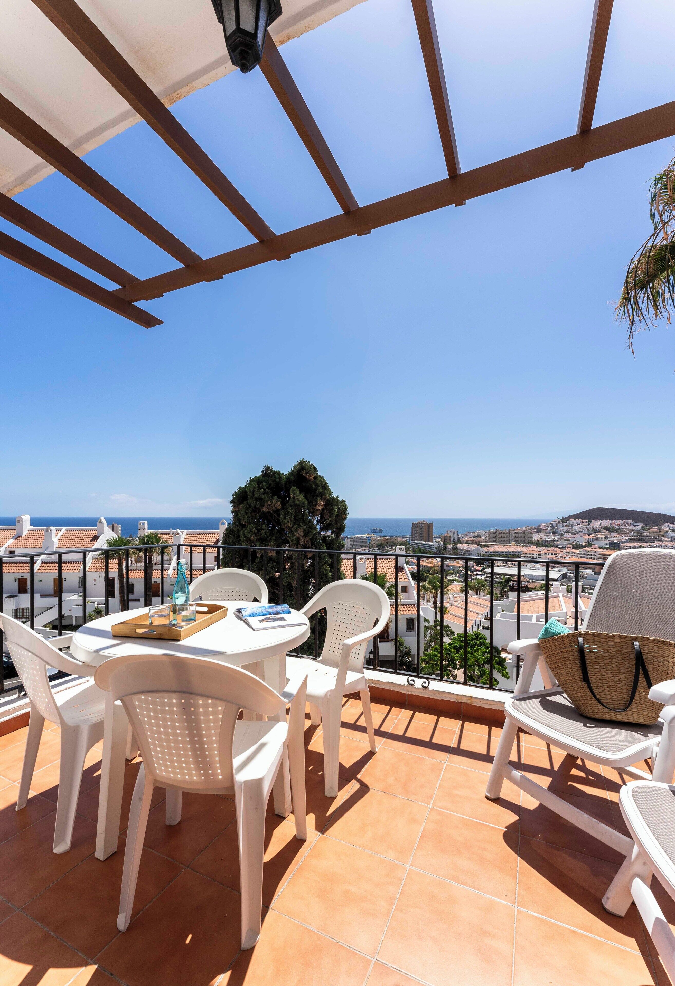 Una terraza con mesa y sillas, vista al mar y un paisaje urbano de fondo.