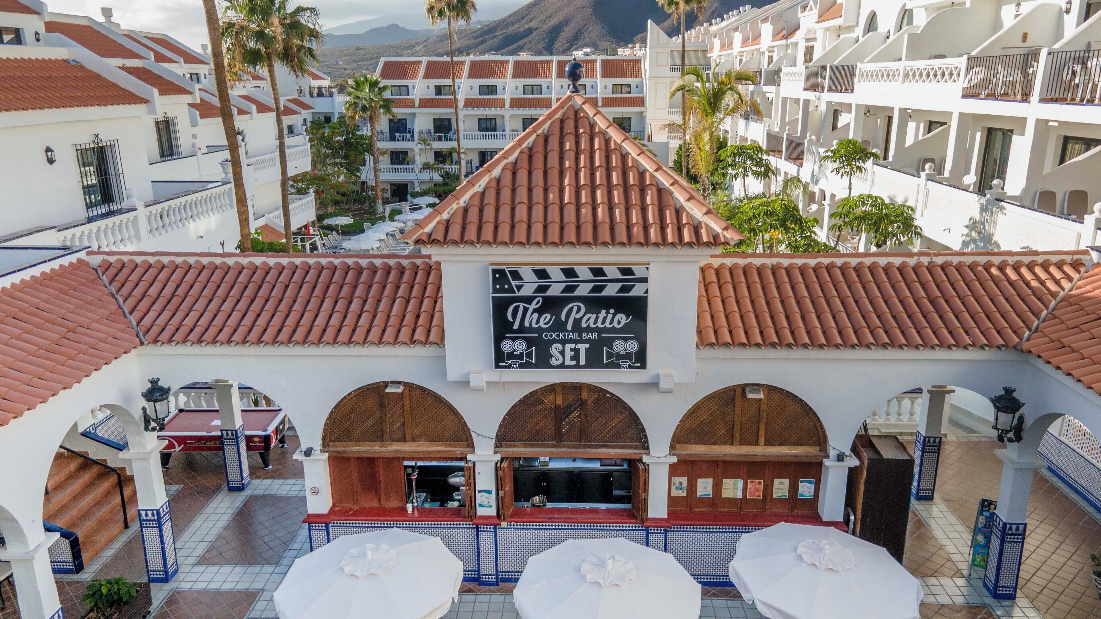 A rooftop bar named "The Patio" with a terrace, palm trees, and a mountainous backdrop.
