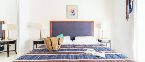 A hotel room with a large bed, two bedside tables with lamps, a woven basket, and a framed picture on the wall.